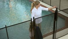 a woman is standing at the edge of a swimming pool and looking out over the railing