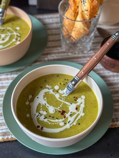 there is a bowl of green soup with cream in it and some crackers on the side