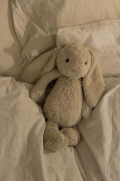 a stuffed animal sitting on top of a bed under a white comforter with sheets