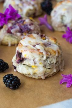 the muffins are covered with icing and blackberries on the table next to flowers