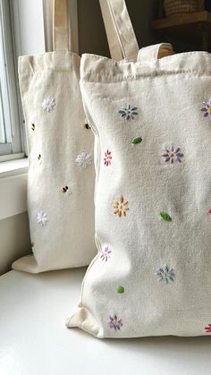 two white bags sitting next to each other on a window sill with flowers painted on them