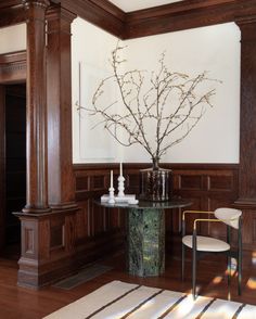 a vase with some branches in it sitting on a table next to a chair and lamp