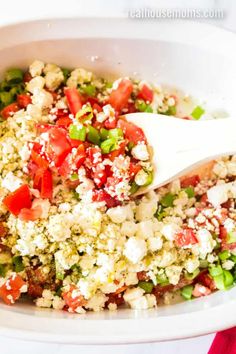 a white bowl filled with chopped vegetables and feta cheese being spooned into it