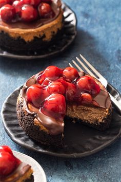 a chocolate cheesecake topped with cherries on top of a black plate next to a fork