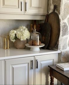 a kitchen with white cabinets and wooden cutting boards on the counter top next to a vase filled with flowers