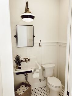 a white toilet sitting next to a sink in a bathroom under a mirror and light