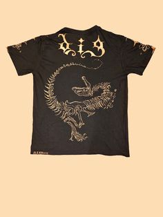 Get ready to stand out in style with this black tee featuring a striking dinosaur design! Hand-painted with bleach on soft cotton, it's a statement piece that's sure to turn heads. 🦖 The front depicts a dinosaur skull and a couple bone tails, while the back features a full skeleton with "DIG" in a gothic font. 🌟 Intricate flowers and stars adorn the sleeves, adding a touch of whimsy to this grunge-inspired shirt! 🌟 Men's U.S. Small 🌟 100% cotton 🌟 Relaxed fit Fitted Acid Wash T-shirt With Graphic Print, Cotton Dinosaur Print Tops For Streetwear, Casual Acid Wash T-shirt With Skull Print, Casual Dinosaur Print Tops For Streetwear, Acid Wash Skull Print Graphic Tee, Acid Wash Graphic Tee With Skull Print, Black Dinosaur Print Crew Neck Top, Black Dinosaur Print Short Sleeve T-shirt, Black Short Sleeve T-shirt With Dinosaur Print