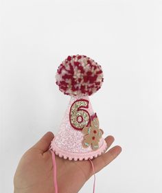 a hand holding a small pink hat with gold sequins and numbers on it