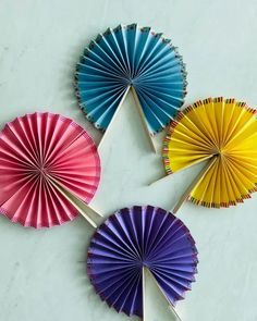 four colorful paper fans sitting on top of a white table next to a cupcake