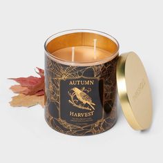 the autumn harvest candle is next to an orange leaf and a gold tin with a black label on it