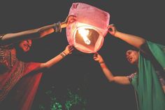 three women are holding up a paper lantern in the air with a glowing light inside