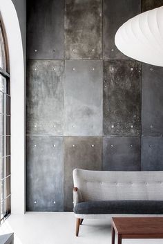 a couch sitting in front of a window next to a wooden coffee table and wall