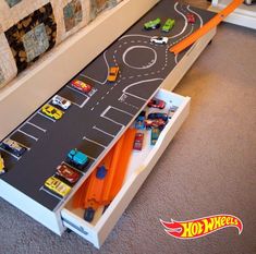 a toy car race track with cars and trucks on the floor next to a bed