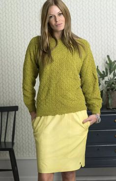 a woman standing in front of a dresser wearing a green sweater and yellow pencil skirt