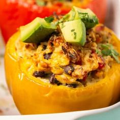 three stuffed peppers with different toppings in them on a white plate next to tomatoes and avocado