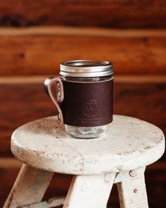 a mason jar sitting on top of a wooden stool with a leather strap around it