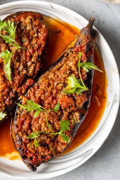 two eggplant stuffed with meat and garnish on a white plate