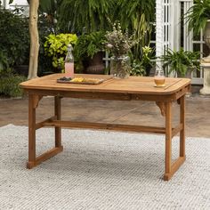 a wooden table sitting on top of a white rug in front of a green house