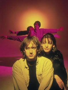 three people sitting on the ground in front of an orange and pink background with one person standing behind them