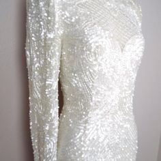 a white dress with sequins on it is hanging up next to a wall