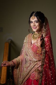 a woman in a red and gold bridal outfit with jewelry on her head, smiling at the camera