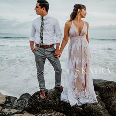 a man and woman holding hands while standing on rocks near the ocean