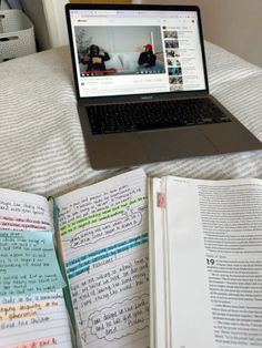 an open book sitting on top of a bed next to a laptop computer