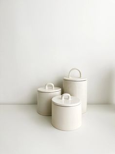 three white canisters sitting on top of a table next to each other in front of a wall