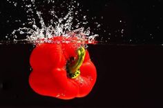 a red pepper is splashing into the water with its head above the water surface