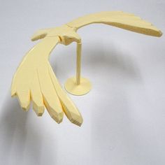 a yellow bird figurine on a white surface with one wing extended to the ground