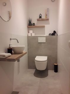 a white toilet sitting in a bathroom next to a sink under a mirror on a wall