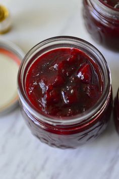 two jars filled with jam sitting on top of a white table next to some spoons