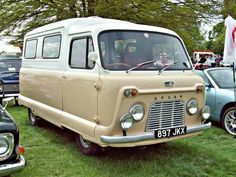 an old van is parked in the grass near other cars and people are looking at it