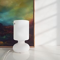 a white lamp sitting on top of a table next to a painting