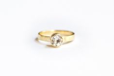 a yellow gold ring with a white diamond in the center on a white background,