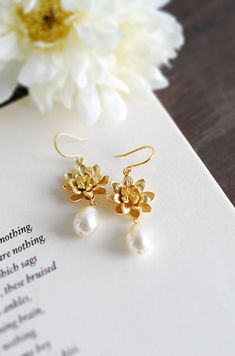 "Gold Lotus and Cream Teardrop Pearl Earrings. Beautiful and classic, these earrings are created from delicate matte gold plated over brass lotus and Swarovski cream teardrop pearls. The total length of these earrings is approx. 1.7\" (43mm) Gold lotus: 17mm across in beautiful matte gold finish Ear wires: tarnish resistant matte gold plated over brass hooks If you would like these Swarovski pearls in a different color, please feel free to contact me for a custom listing. ♥ Click the link below Bridal Gold Earrings, Teardrop Pearl Earrings, Yoga Lotus, Jewellery Photography Inspiration, Creative Jewelry Photography, Dangle Earrings Wedding, Jewelry Photography Styling, Lotus Jewelry, Gold Lotus