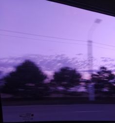 the view from inside a bus looking out at trees and buildings in the distance with purple hues