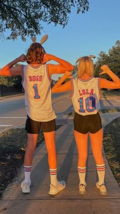 two women in basketball uniforms are standing on the sidewalk with their arms around each other