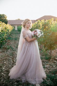 a woman in a wedding dress is standing in the grass with her bouquet and looking off into the distance