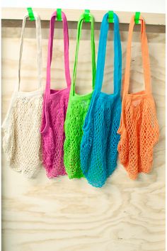 four different colored bags hanging up on a wooden wall with green handles and two pink, one orange, one blue