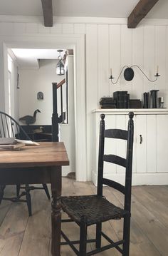 a wooden chair sitting next to a table in a room with white walls and wood floors