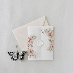 an envelope with a butterfly on it next to a button and flowered card holder