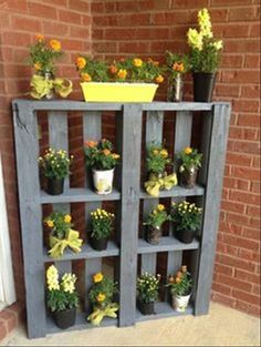 a wooden shelf filled with potted plants next to a brick wall