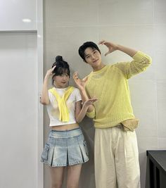 two young people standing next to each other in front of a white wall and black counter