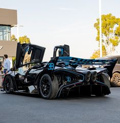 a black and blue race car parked in front of a building with its doors open