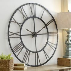 a large metal clock mounted to the side of a white wall next to a lamp