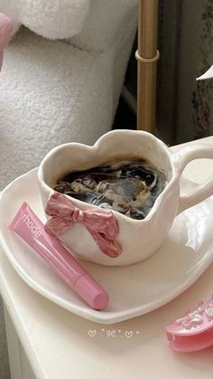 a white plate topped with a heart shaped cup filled with liquid next to two pink toothbrushes