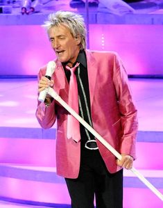 an older man in a pink suit holding a microphone and singing into a white mic