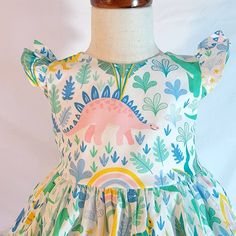 This little pastel dinosaur dress features multi colored dinosaurs in a tropical jungle setting on a cream colored background . It would be perfect for a dinosaur themed birthday party or for any little one that loves dinos! The bodice is lined with soft cotton and it snaps in the back with Kam snaps for easy on and off. There are matching fabric tie backs that tie into a bow in the back of the dress for a perfect fit around the waist and the bow adds to the festive look of this little party dre Dinosaur Dress, Dinosaur Themed Birthday Party, Kam Snaps, Dress Pastel, Baby Dinosaur, Dino Birthday, Colored Background, Dress For Girls, Birthday Dress