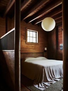 a bed sitting under a window in a bedroom next to a wooden wall and floor